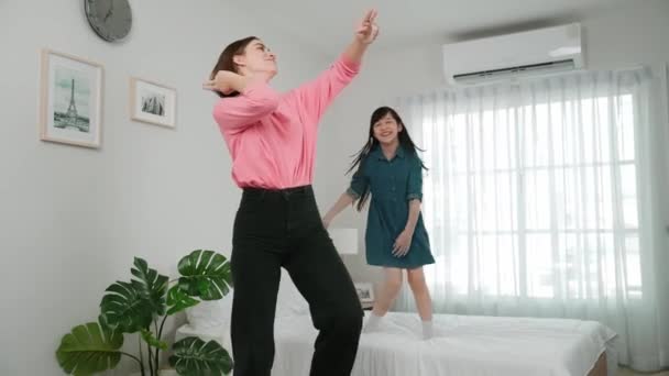 Boldog vonzó anya táncol zenére együtt ázsiai lánya a hálószobában. Kaukázusi anya tánc vagy testmozgás, míg aranyos gyermek mozog a zene, miközben ugrik az ágyba. Családi kikapcsolódás. Pedagógia. - Felvétel, videó