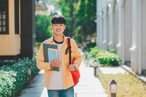 Feliz estudiante sonriente con libro en la mano en el campus mientras va a estudiar para aprender. - Foto, imagen