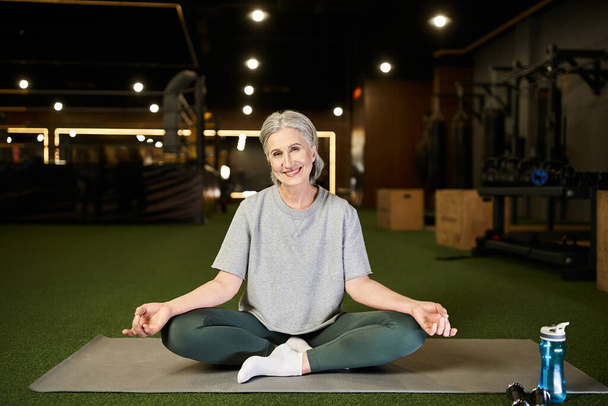 good looking positive mature woman with gray hair in sportswear meditating and looking at camera - Photo, Image