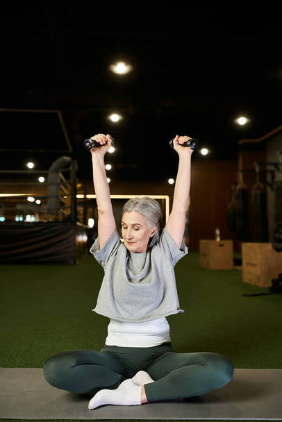 fröhliche attraktive, reife Sportlerin mit grauen Haaren, die im Fitnessstudio aktiv mit Kurzhanteln trainiert - Foto, Bild