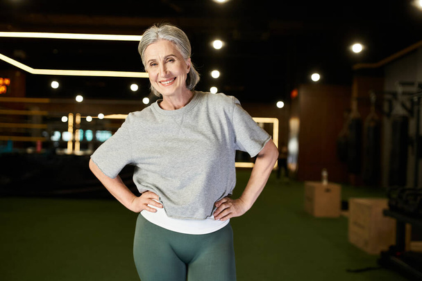beautiful mature positive woman in cozy sportswear posing with arms akimbo and smiling at camera - Photo, Image