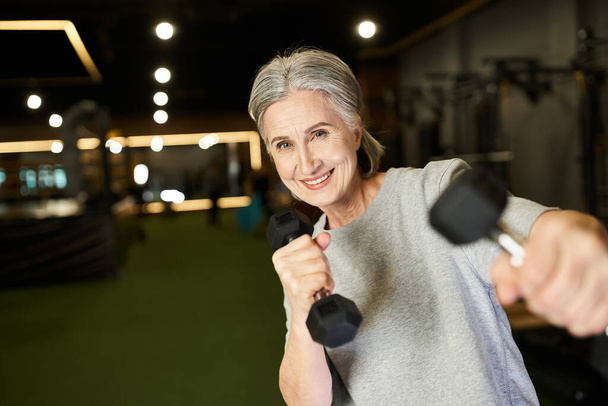 attraktive, fröhliche Seniorin im Sportkleidungstraining aktiv mit Hanteln und lächelnd in die Kamera - Foto, Bild