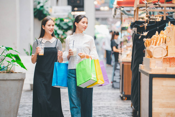 Δύο γυναίκες περπατούν στο δρόμο με τσάντες για ψώνια. Μια από τις γυναίκες κρατάει μια πράσινη τσάντα. - Φωτογραφία, εικόνα