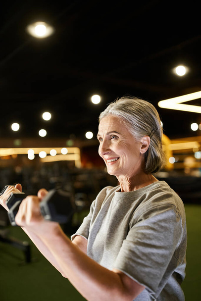 hyvännäköinen vanhempi nainen viihtyisissä urheiluvaatteissa, jotka käyttävät aktiivisesti käsipainoja kuntosalilla - Valokuva, kuva