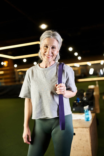 Fröhliche Seniorin in Sportbekleidung posiert aktiv mit Fitness-Expander und lächelt in die Kamera - Foto, Bild