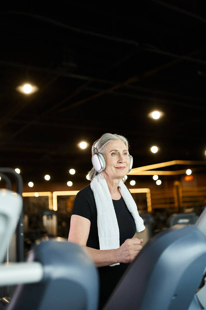 wesoły siwy seniorka w odzieży sportowej trening na bieżni i słuchanie muzyki w słuchawkach - Zdjęcie, obraz