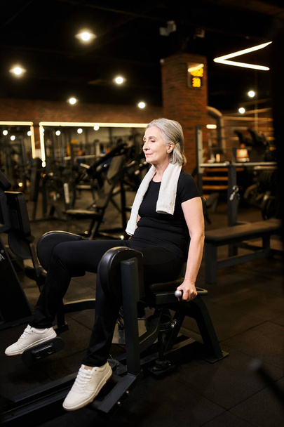 dobrze wyglądający wesoły starszy kobieta w odzieży sportowej szkolenia aktywnie na łydki maszyny podczas gdy w siłowni - Zdjęcie, obraz