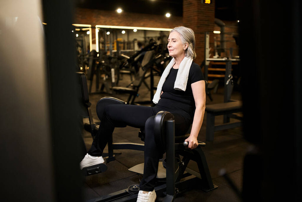beautiful senior jolly sportswoman with gray hair and towel training on calf machine while in gym - Photo, Image
