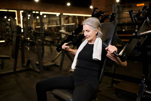 atrakcyjna starsza kobieta w przytulnej odzieży sportowej z siwymi włosami trening na maszynie do prasowania klatki piersiowej w siłowni - Zdjęcie, obraz