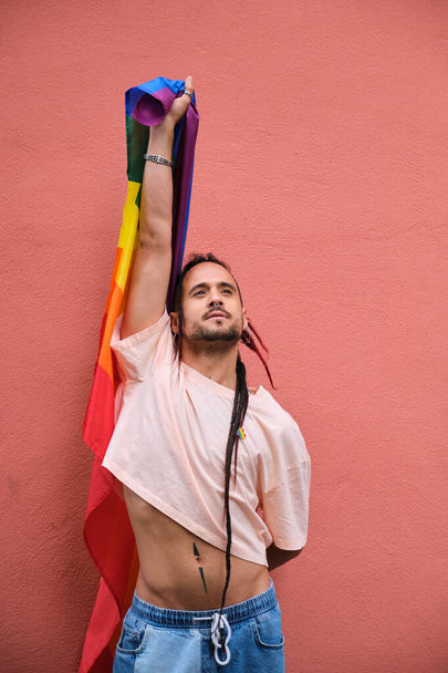 Гей с дредами держит радужный флаг и гордо улыбается. Концепция гордости и счастья. - Фото, изображение