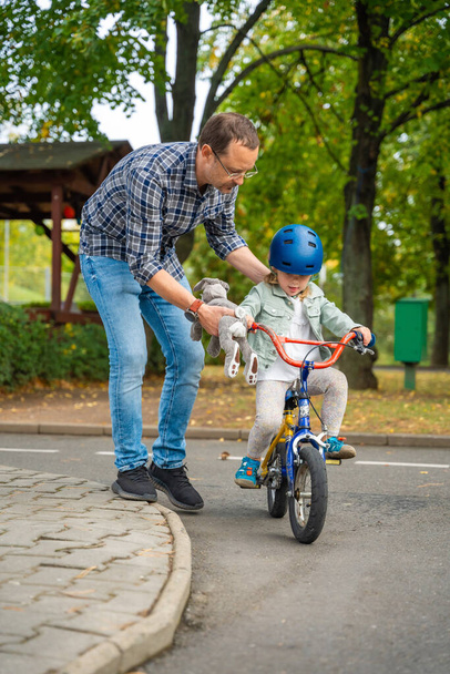 Young father teaches child daughter to ride public bike on one of traffic playground in Prague, Czech republic. High quality photo - Photo, Image