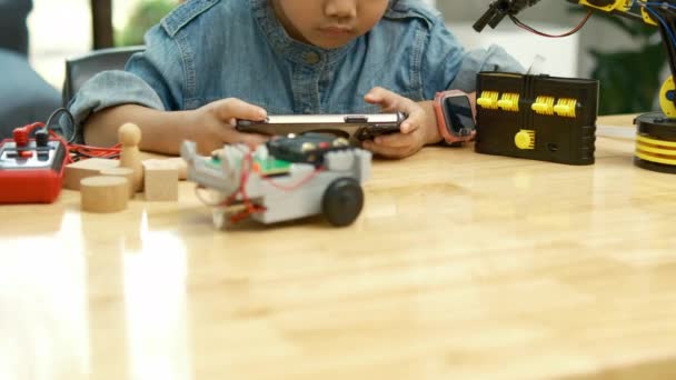 Een jong Aziatisch meisje in een STEM-klasse aandachtig gebruik maakt van een smartphone app op afstand te bedienen van een speelgoedauto, presentatie van tech-onderwijs. - Video