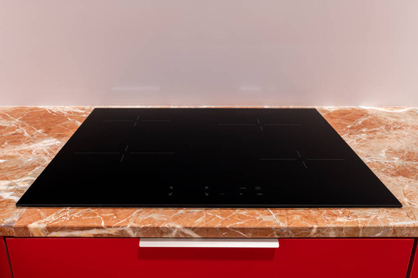An uncluttered shot of an induction stove integrated into a marble countertop with vibrant red cabinets - Photo, Image