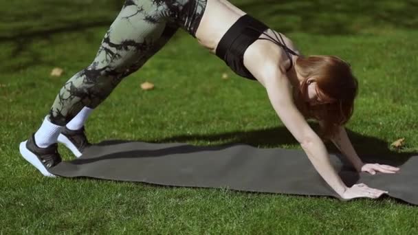 Mladá atletická dívka cvičení na podložce na zelené trávě - Záběry, video