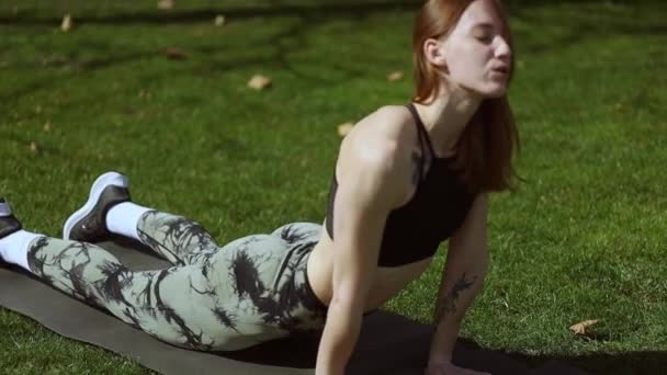 Mladá atletická dívka cvičení na podložce na trávě - Záběry, video