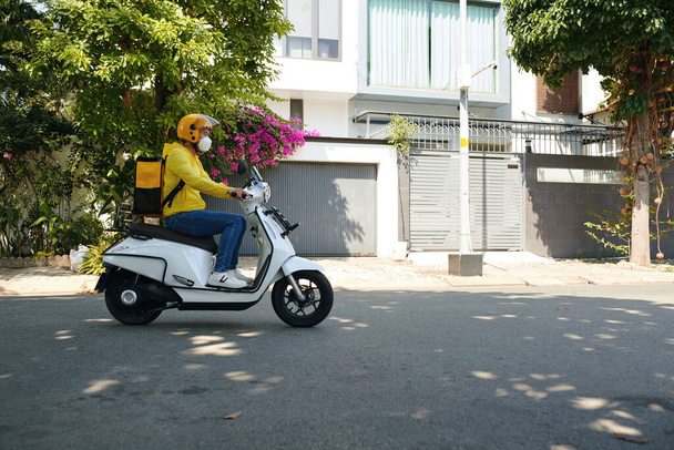 Entrega hombre con gran bolsa de montar en moto, vista lateral - Foto, imagen