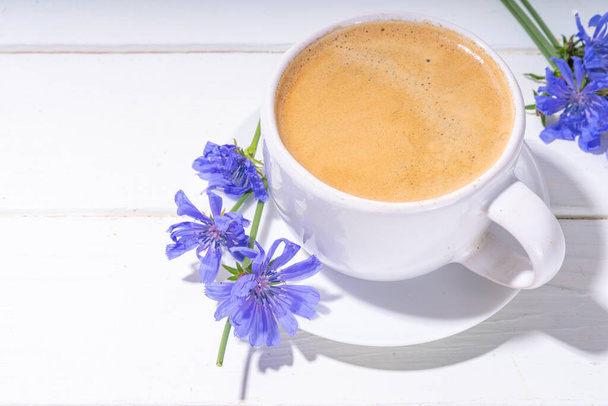 白い木製のテーブルの上にチコリハーブコーヒードリンクと青の花。チコリの花と根の粉と代替ビーガンとケトダイエットコーヒー  - 写真・画像