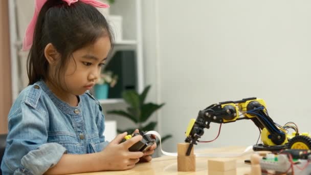 Egy általános iskolás lány egy távirányítós robotkar működtetésére összpontosít, bemutatva a STEM oktatást akcióban.. - Felvétel, videó
