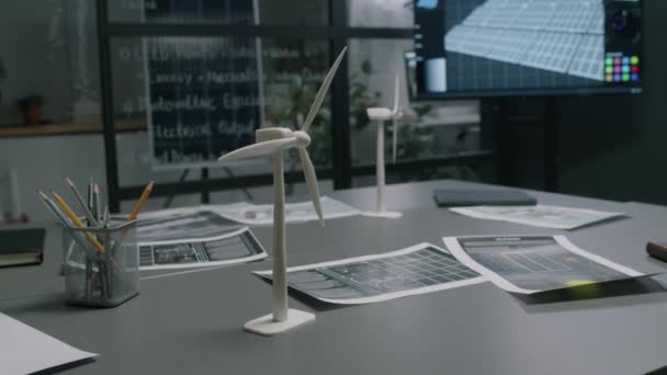 No hay imágenes de personas de mesa con prototipos de molino de viento cerca de múltiples documentos en la moderna oficina de energía alternativa con pantalla multimedia y pared de vidrio - Metraje, vídeo