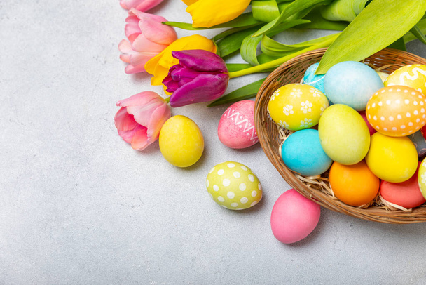 Húsvéti kosár tele színes tojásokkal és egy csokor tulipánnal egy texturált fa asztalon. Húsvéti ünnepség koncepció. Színes húsvéti kézzel készített díszített húsvéti tojás. Helyet az sms-nek. Fénymásolási hely - Fotó, kép