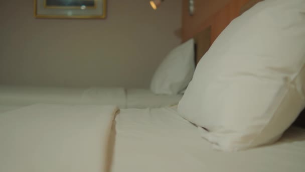 Primo piano di un letto ben fatto con lenzuola bianche e morbidi cuscini in una camera d'albergo illuminata durante la notte - Filmati, video