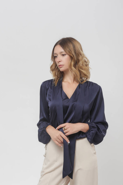 Serie studiofoto 's van jong vrouwelijk model met donkerblauwe zijden satijnen blouse en crème broek - Foto, afbeelding