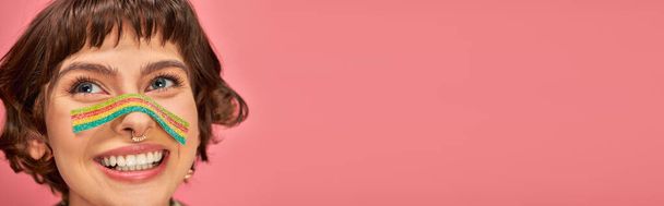 happy woman in her 20s with sweet and sour candy strip aon her nose on pink background, banner - Photo, Image