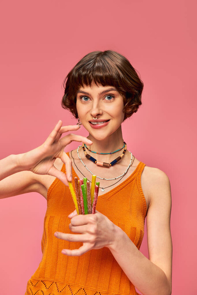 Mutlu piercingli kız 20 'li yaşlarında gülümsüyor ve elinde bir demet tatlı ve ekşi şekerlemeyle pembe ellerde - Fotoğraf, Görsel
