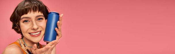 estandarte de alegre joven con pelo corto morena sosteniendo lata de refresco en rosa, bebida de verano - Foto, Imagen