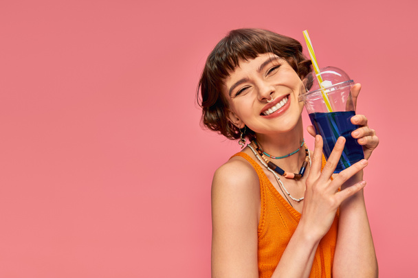 cheerful young woman with short brunette hair posing with refreshing summer cocktail on pink - Fotografie, Obrázek