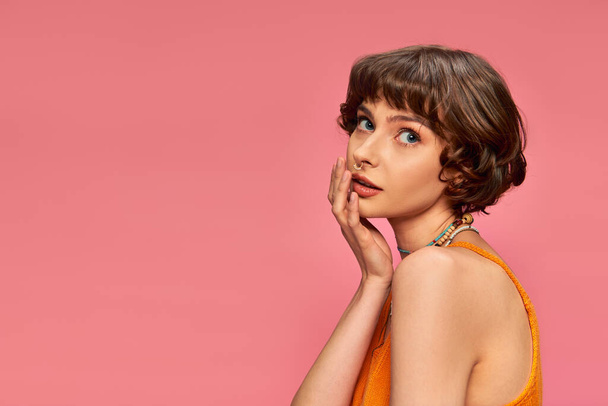 pretty young woman in her 20s with short hair in vibrant tank top posing on pink background - Photo, Image