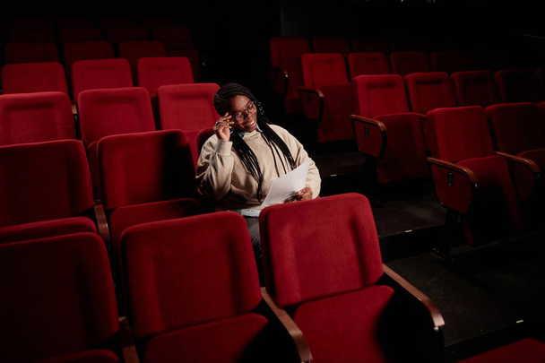 劇場コピースペースで空っぽの聴衆に座っている間,笑顔のアフリカ系アメリカ人女性の肖像画 - 写真・画像