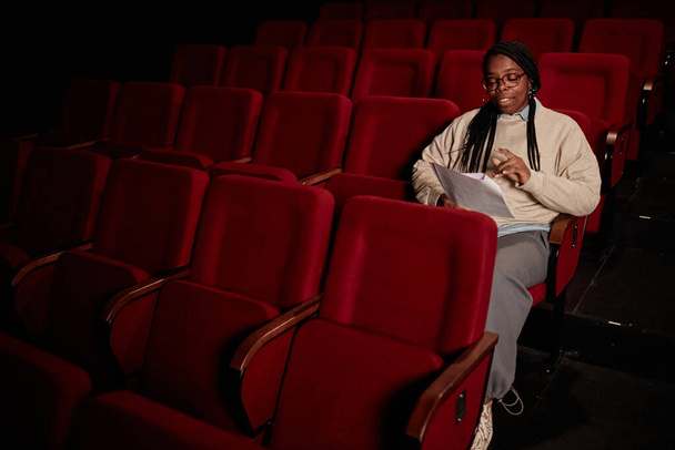 Minimales Porträt einer erwachsenen schwarzen Frau, die im Theater im Kopierraum bei schwachem Licht Skript liest - Foto, Bild