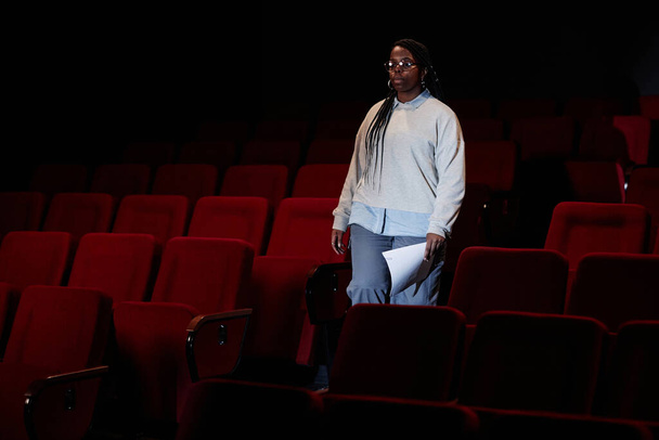 Retrato dramático de la artista femenina caminando hacia el escenario en público de teatro vacío con espacio de copia de poca luz - Foto, imagen