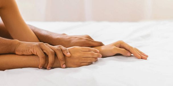 Juegos sexuales. Manos de pareja afroamericana haciendo el amor en la cama, panorama, espacio libre
 - Foto, imagen