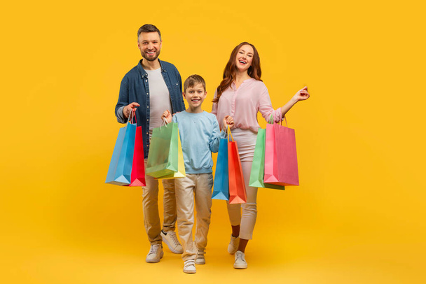 A kép tartalmaz egy boldog család két felnőtt és egy gyermek gazdaság színes bevásárló táskák, pózol egy világos sárga háttér - Fotó, kép