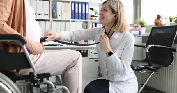 Femme écoute ventre avec stéthoscope à la femme enceinte en fauteuil roulant. grossesse et maternité en fauteuil roulant concept - Séquence, vidéo