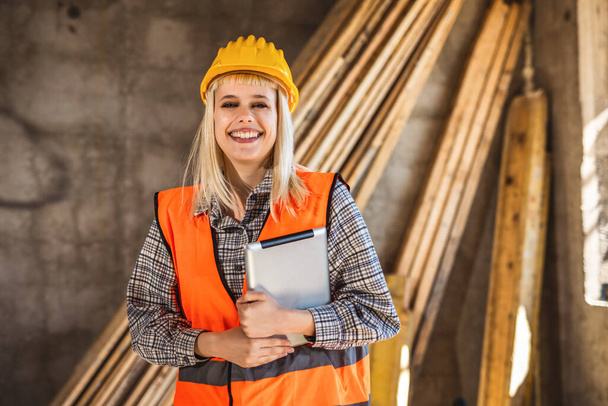 Portrait d'une femme constructeur prospère portant un casque jaune et un gilet jaune de sécurité. Portrait d'architecte debout sur le chantier et regardant la caméra. - Photo, image