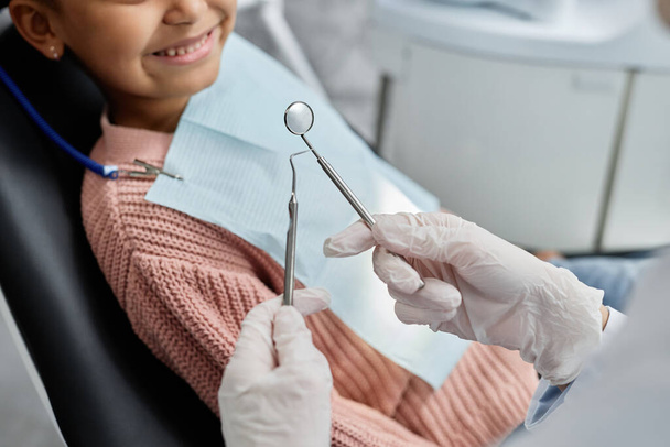 Nahaufnahme einer Zahnärztin, die Werkzeuge hält, während sie mit Kind in Zahnklinik arbeitet, Kopierraum - Foto, Bild