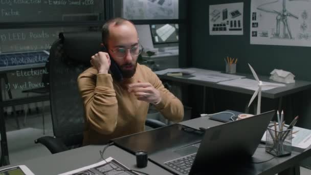 Çift taraflı yenilenebilir enerji tasarrufu CEO 'sunun bilgisayarda çalışırken telefonla konuştuğu ve modern ofiste grafik tablet kullanırken gece duvarlarında planlar olduğu orta büyüklükte görüntüler. - Video, Çekim