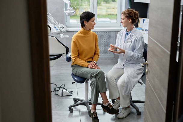 Портрет зрілої жінки, що розмовляє з стоматологом у стоматологічній клініці та консультує з імплантації зубів, копіює простір - Фото, зображення