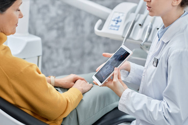 Close-up de dentista do sexo feminino mostrando imagens de raios X em tablet para paciente do sexo feminino na clínica, espaço de cópia - Foto, Imagem