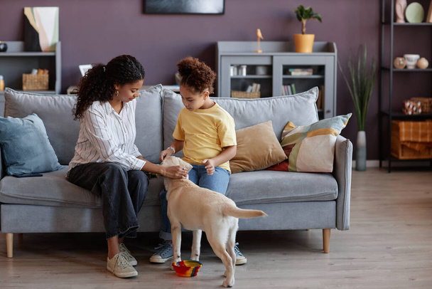 Full length portrait of mother and daughter playing with puppy in cozy home interior, copy space - Photo, Image