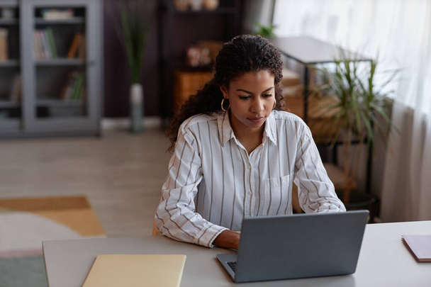Vorderseite Porträt einer schwarzen jungen Frau mit Laptop, während sie von zu Hause aus in gemütlicher Umgebung arbeitet, Kopierraum - Foto, Bild