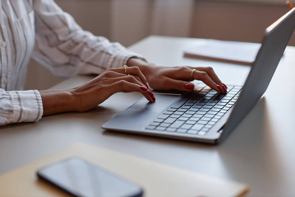Πλευρική άποψη closeup αγνώριστη μαύρη γυναίκα χρησιμοποιώντας φορητό υπολογιστή με έμφαση στην κομψή γυναικεία δακτυλογράφηση χέρια στο πληκτρολόγιο - Φωτογραφία, εικόνα