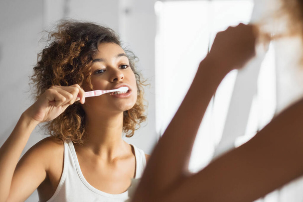 Opieka stomatologiczna. Młoda Afro Woman szczotkująca zęby w łazience rano. Panorama, ostrość selektywna - Zdjęcie, obraz