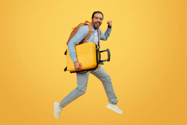 スーツケースで飛躍するエネルギッシュなインド人男性,旅行のための喜びと興奮を表現 - 写真・画像