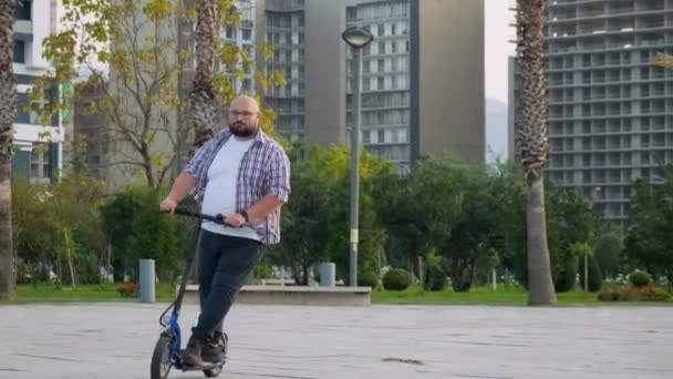 Hombre de talla grande montando e-scooter en la ciudad. Hombre conduciendo scooter eléctrico al aire libre. Transporte eléctrico y ecológico. Transporte ecológico. concepto de estilo de vida sostenible. - Imágenes, Vídeo