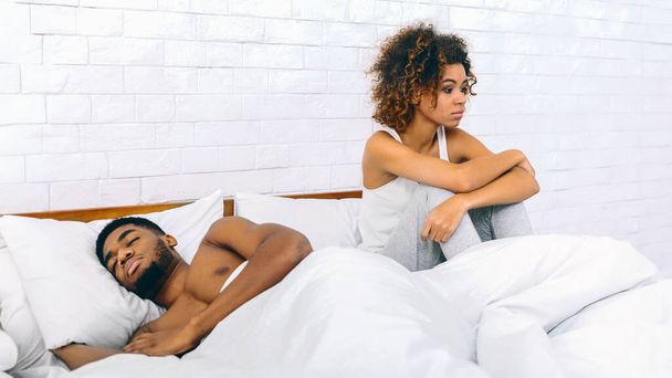 Afro-Amerikaanse vrouw zit apart van haar slapende partner, het overbrengen van emotionele afstand en contemplatie in relaties - Foto, afbeelding