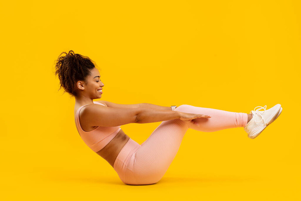 Aktif, Afro-Amerikalı, pembe spor elbiseli bir kadın, sarı arka planda pilates tekniği kullanıyor. - Fotoğraf, Görsel